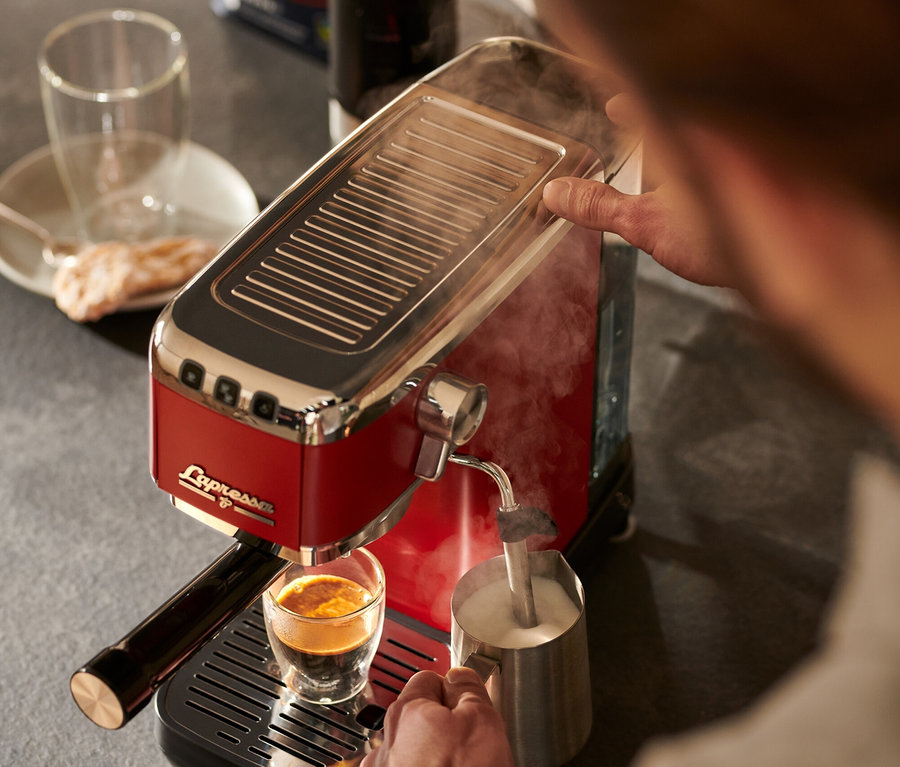 Un homme prépare du café et fait mousser du lait avec une machine à porte-filtre rouge « Lapressa ».