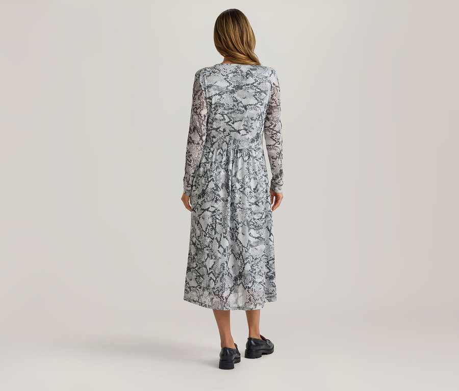 Femme de dos portant une robe midi à manches longues avec un imprimé serpent et des mocassins noirs.