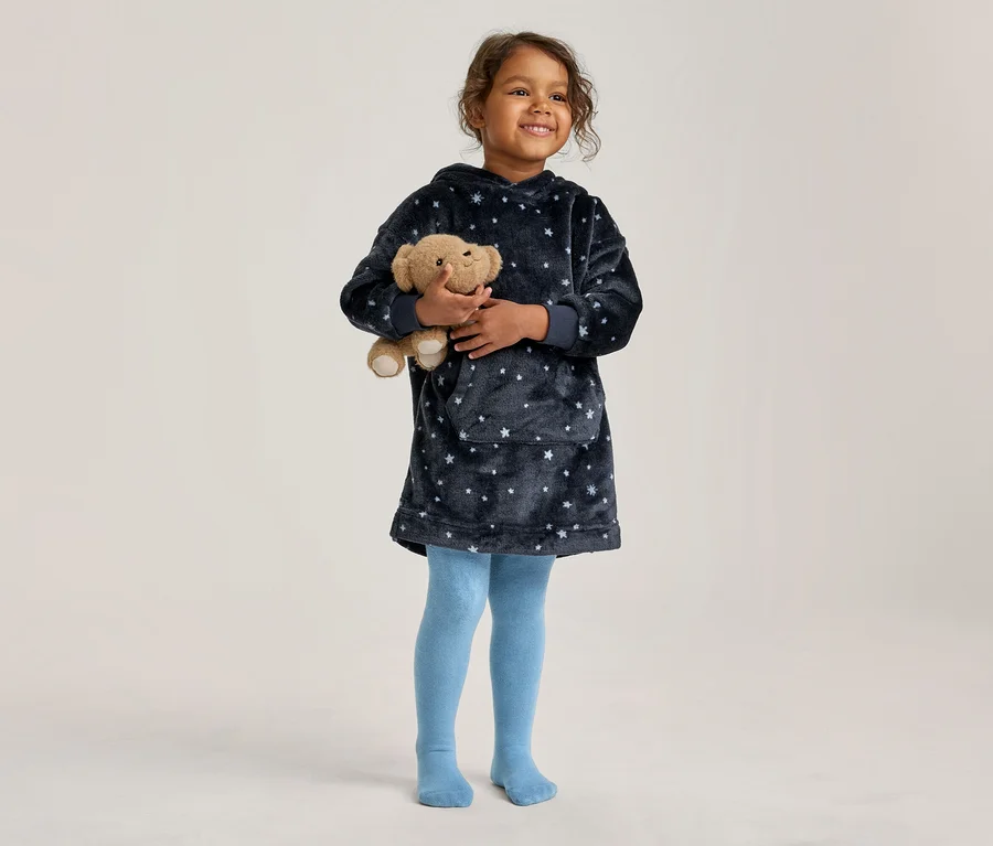 Jeune fille tenant un ours en peluche. Elle porte un sweat-plaid à capuche bleu foncé et moelleux avec des étoiles et des collants bleu clair.