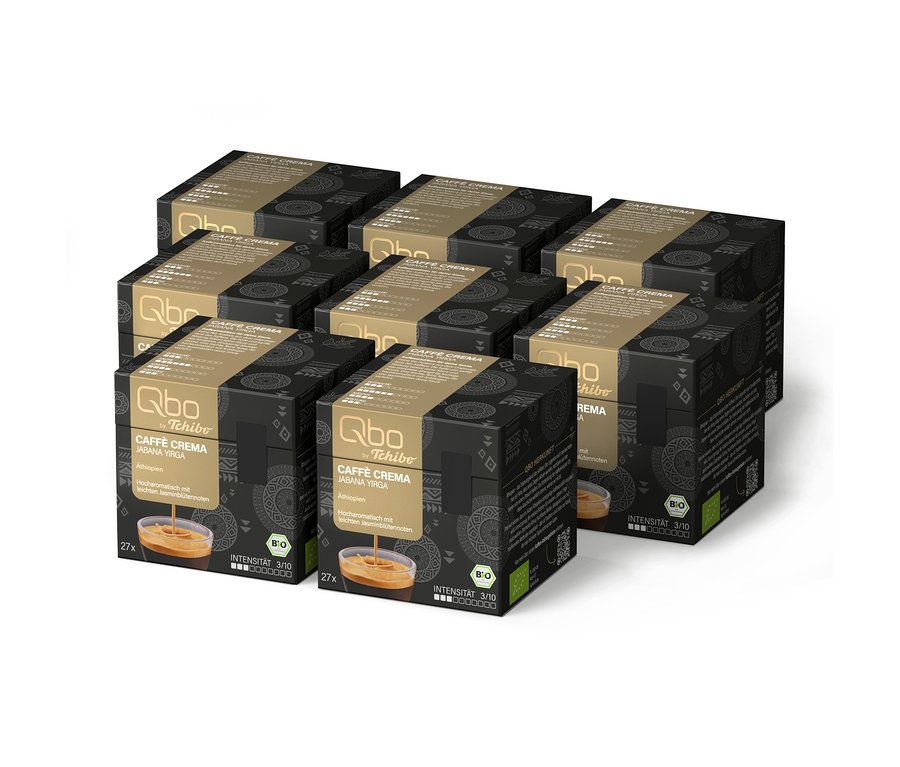 Huit boîtes noires et dorées de capsules de café Qbo by Tchibo Caffè Crema Jabana Yirga, totalisant 216 capsules, sont empilées. Chaque boîte présente des motifs géométriques, les mentions 'Äthiopien', 'Hocharomatisch mit leichten Jasminblütennoten', une intensité de 3/10 et un logo BIO.