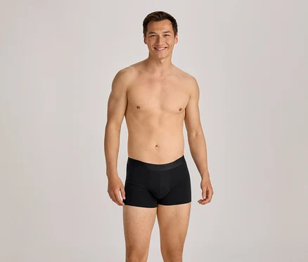 Homme torse nu en boxer noir souriant à la caméra.