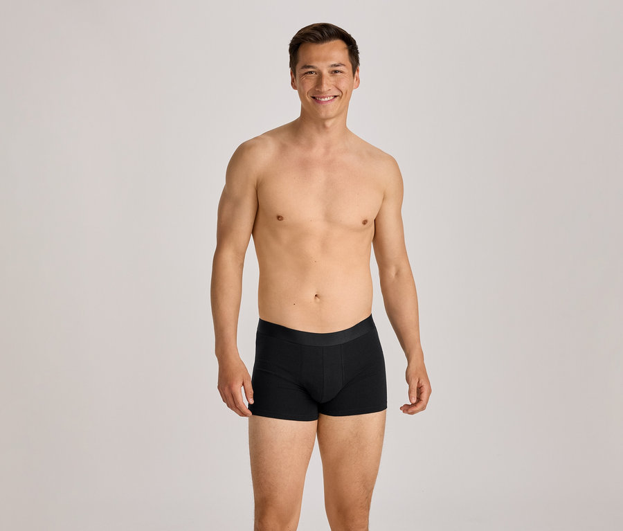Homme torse nu en boxer noir souriant à la caméra.