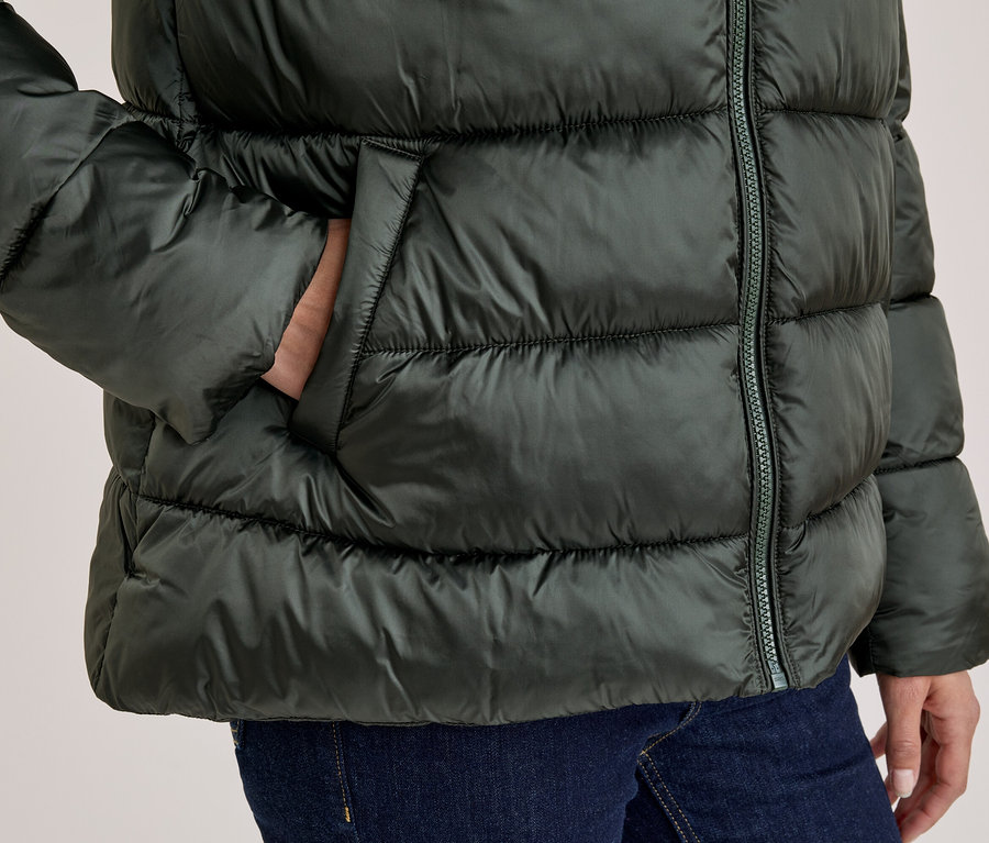 Personne portant une doudoune vert foncé, la main dans la poche, et un jean bleu.
