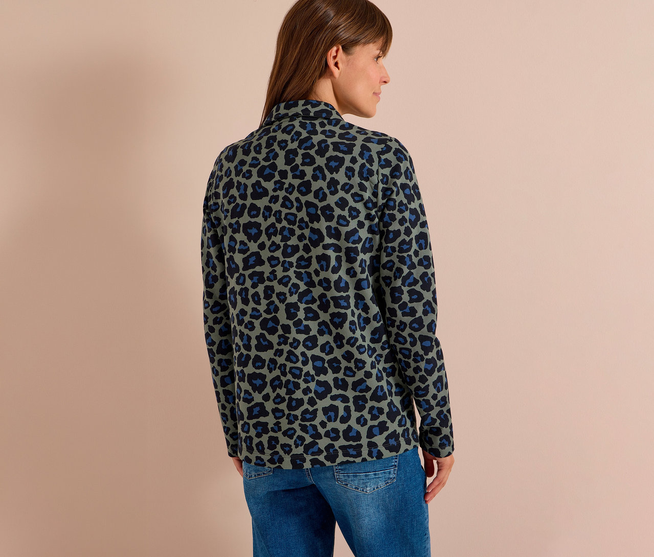Femme de dos, portant un blazer en jersey à imprimé léopard vert, noir et bleu et un jean bleu.