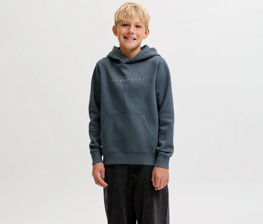 Jeune garçon souriant portant un sweat à capuche Jack&Jones Star gris foncé avec une poche kangourou et un pantalon foncé.