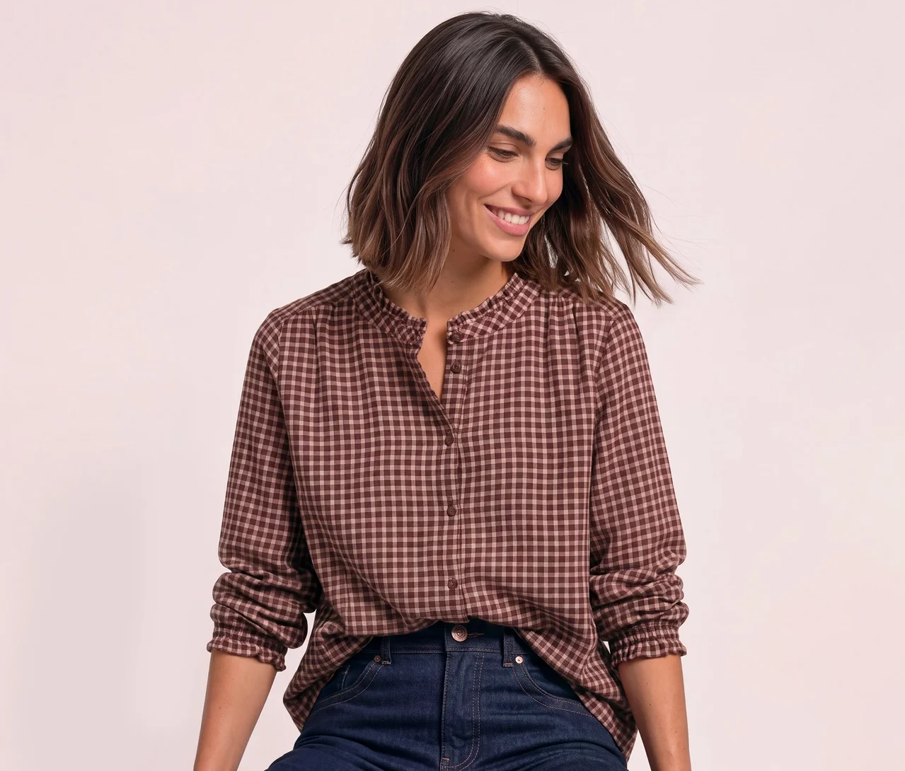 Femme souriante portant une Blouse Street One à carreaux marron et rose clair avec un col à volants et un jean bleu foncé.