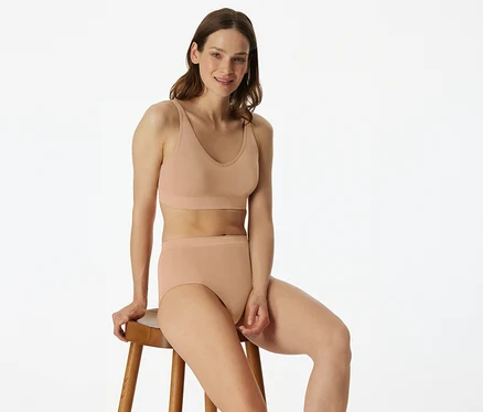 Femme assise sur un tabouret portant une brassière douce SCHIESSER avec coussinets, beige.