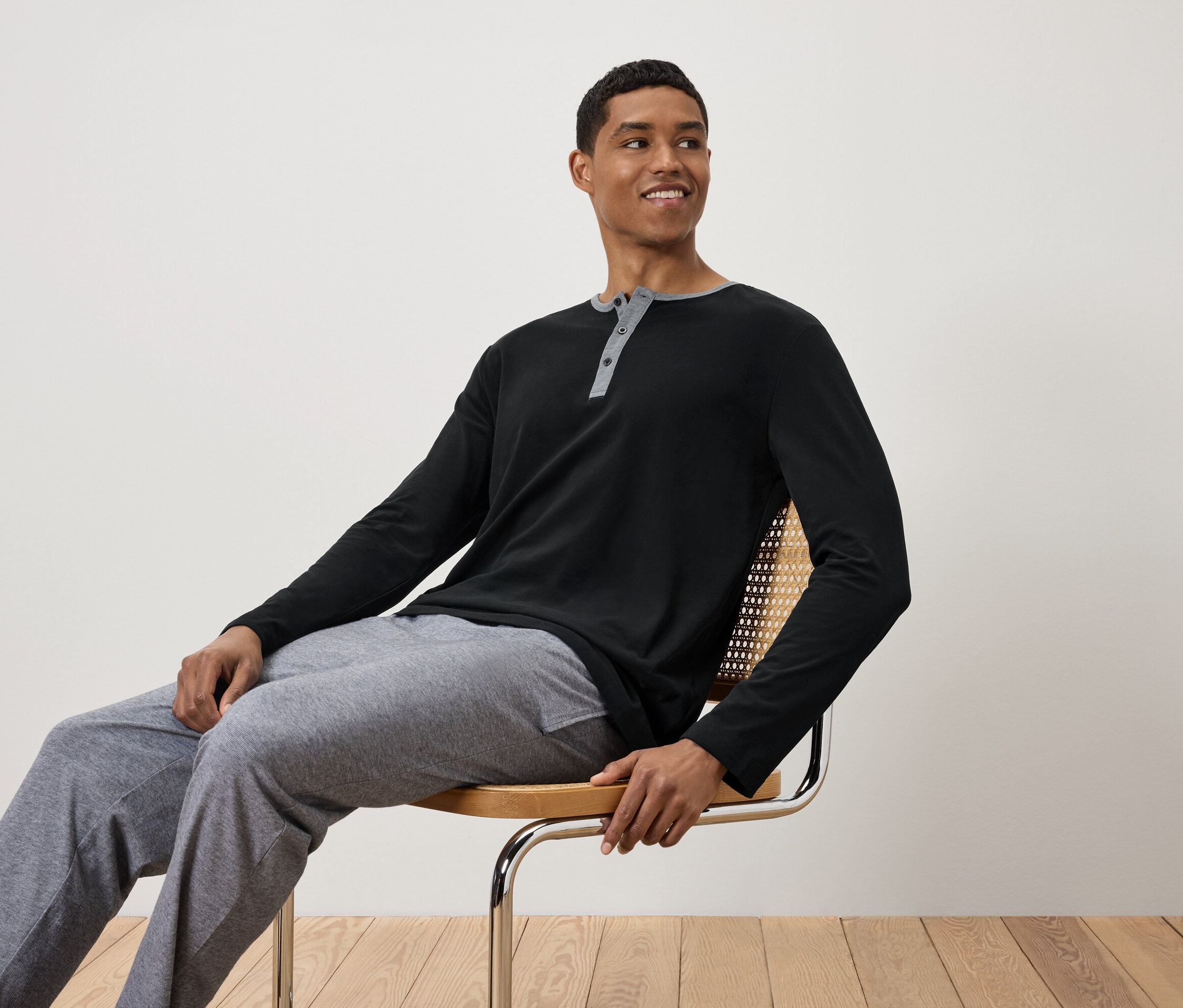 Un homme est assis sur une chaise, portant un t-shirt noir à manches longues et un pantalon de survêtement gris.