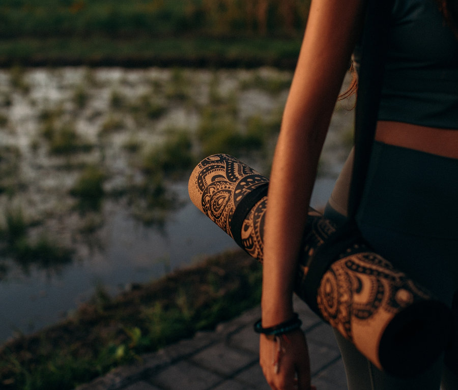 Une femme tient un tapis de yoga avec un motif noir sur un fond de nature.