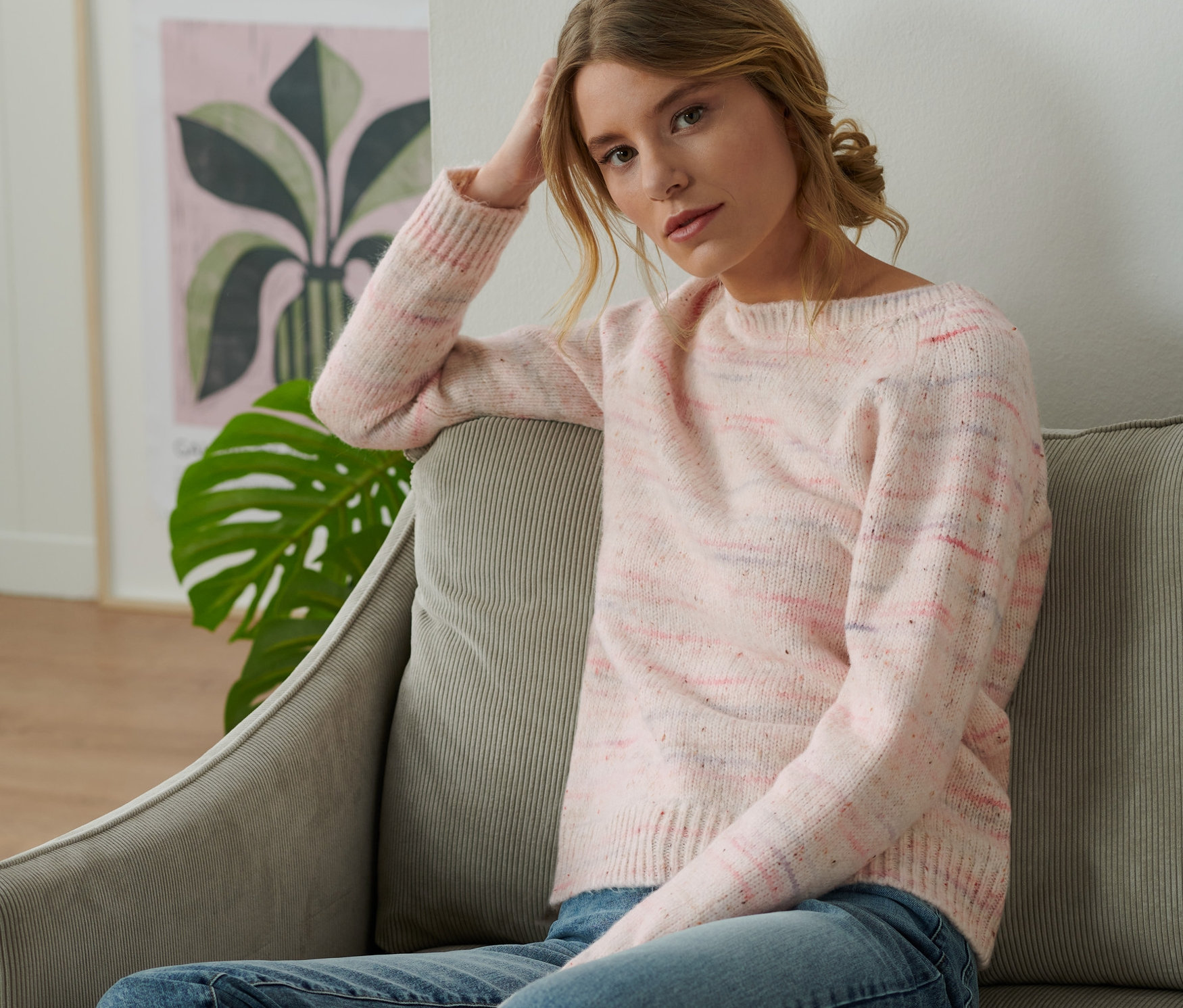 Une femme est assise sur un canapé et porte un pull en grosse maille avec fil d'ornement.