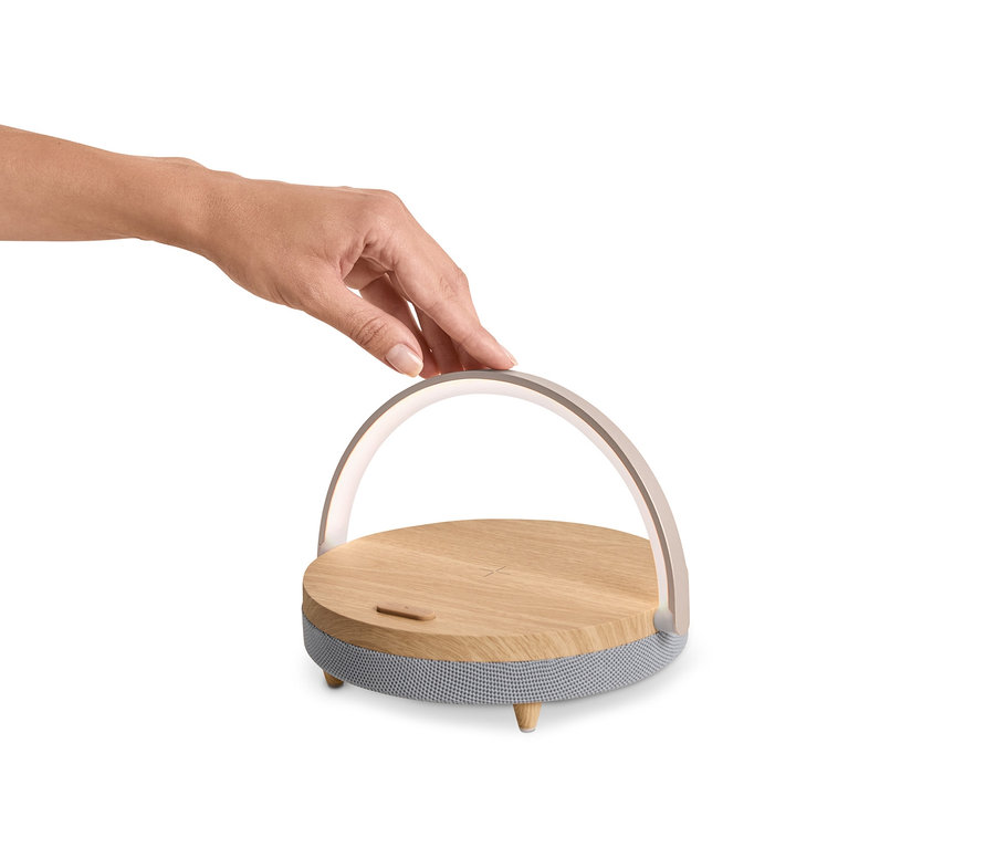 Une main touche un haut-parleur Bluetooth avec chargeur sans fil et veilleuse LED.