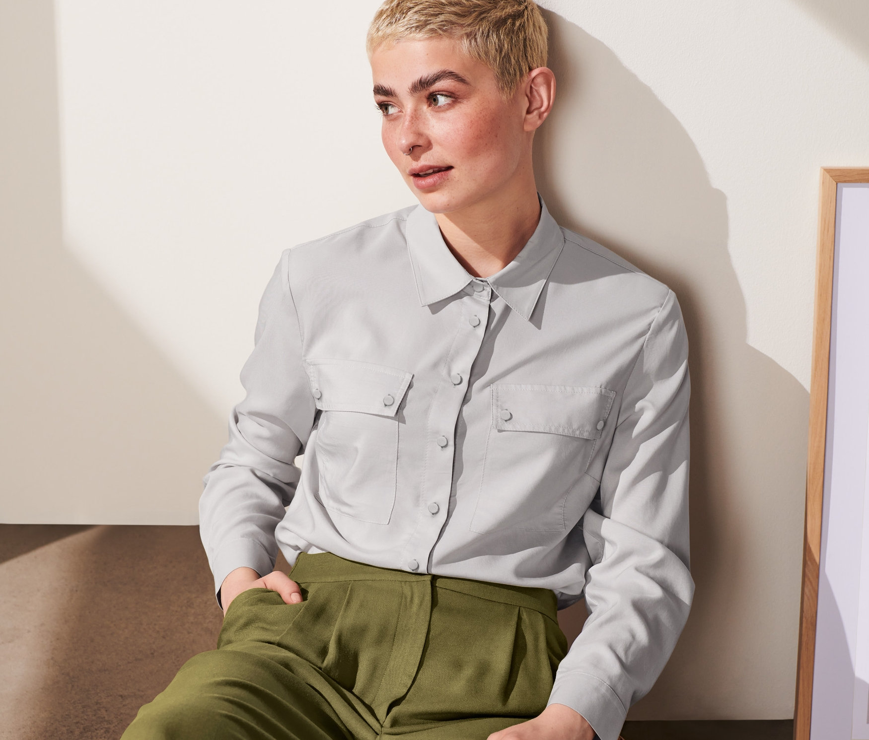 Une femme est assise et porte un chemisier gris clair.