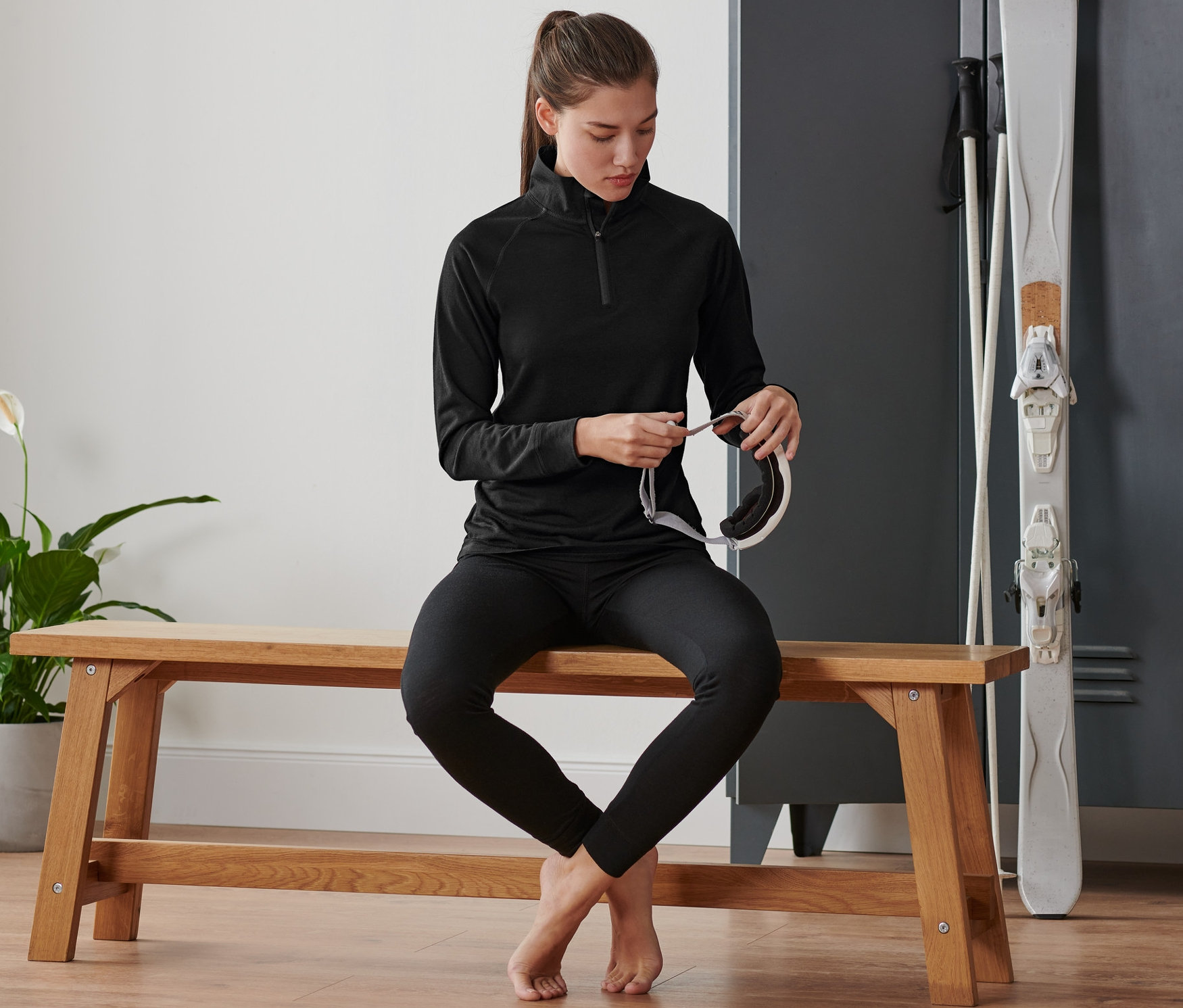 Une femme est assise sur un banc et tient un masque de ski. Elle porte un t-shirt technique avec de la laine mérinos.