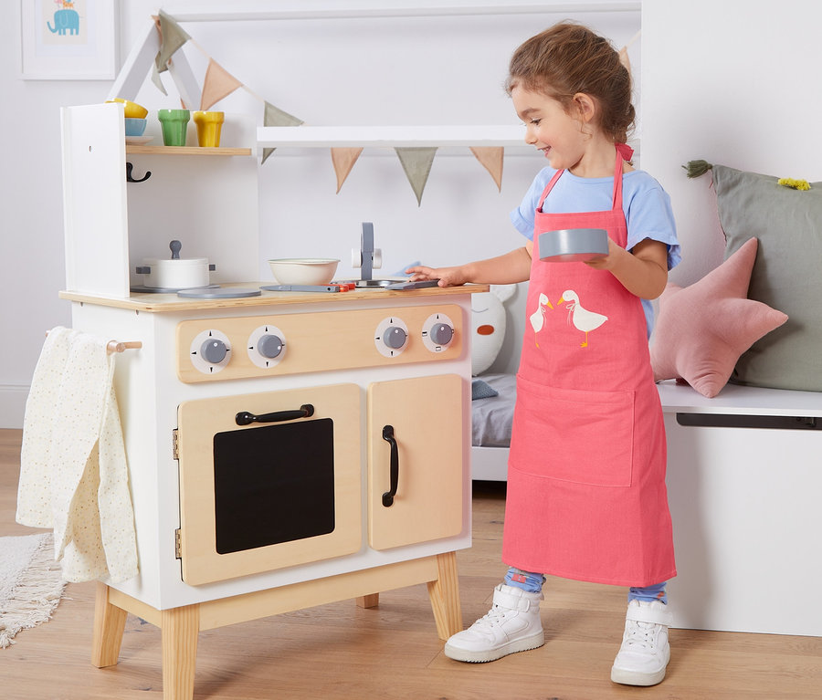 Une fille joue avec une cuisine jouet et porte un tablier pour enfant.