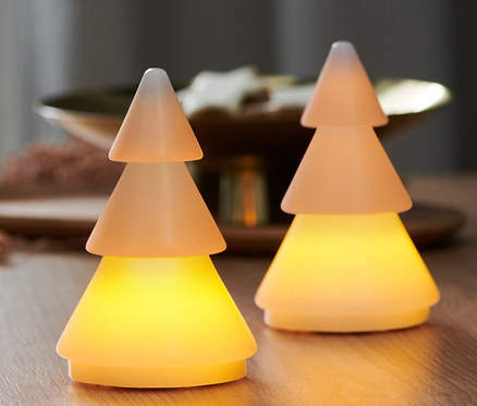 Deux arbres de Noël en cire avec LED sont posés sur une table en bois. Une fenêtre est visible à l'arrière-plan.