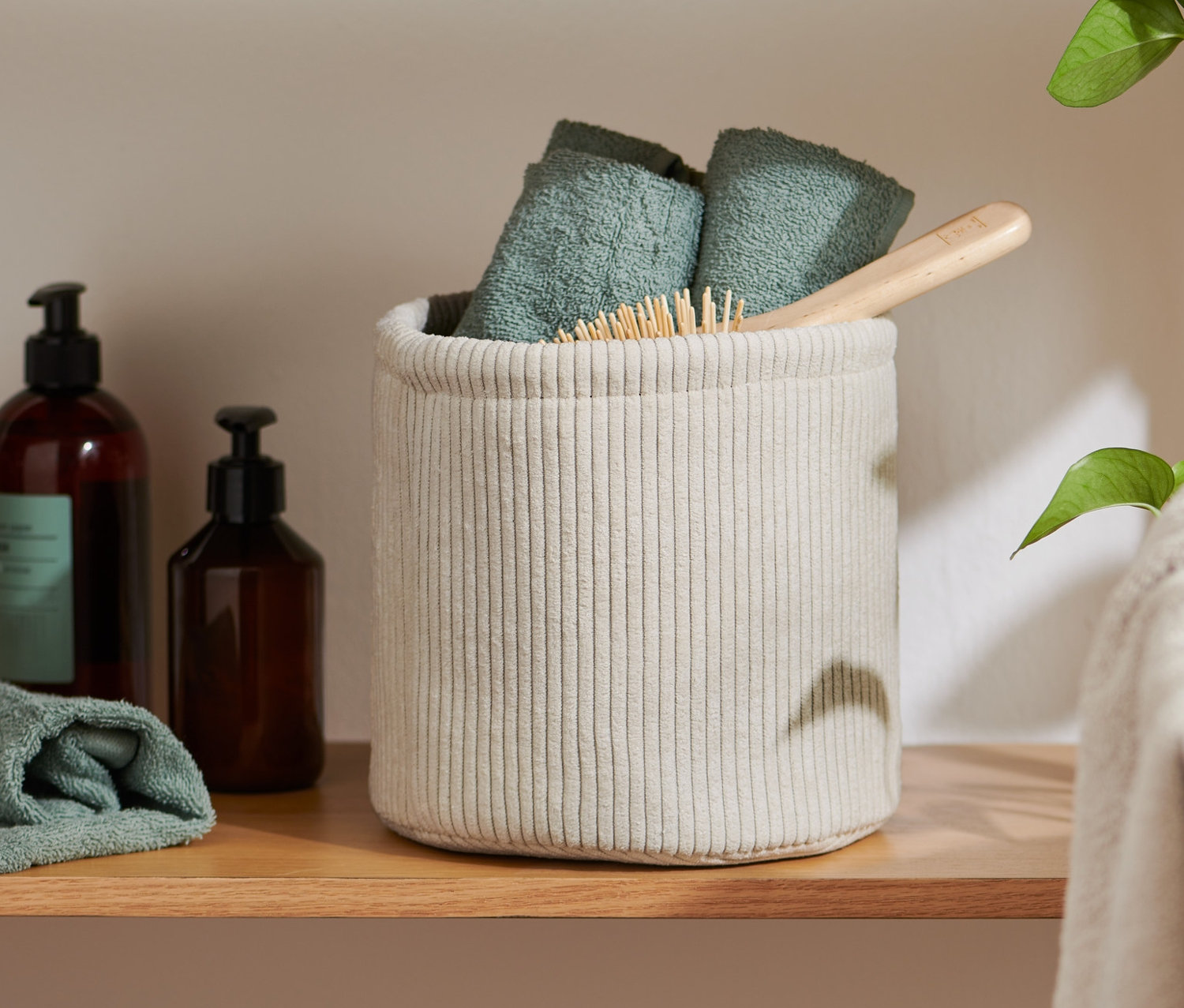 Sur une étagère, un panier de rangement d'environ 20 x 20 x 20 cm contenant des serviettes pliées et une brosse à cheveux.