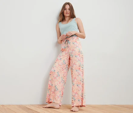 Une femme pose en pantalon relax abricot et débardeur bleu clair.