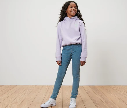 Une fille pose en tregging pour enfant – Fit « Jule », bleu et sweat à capuche violet.