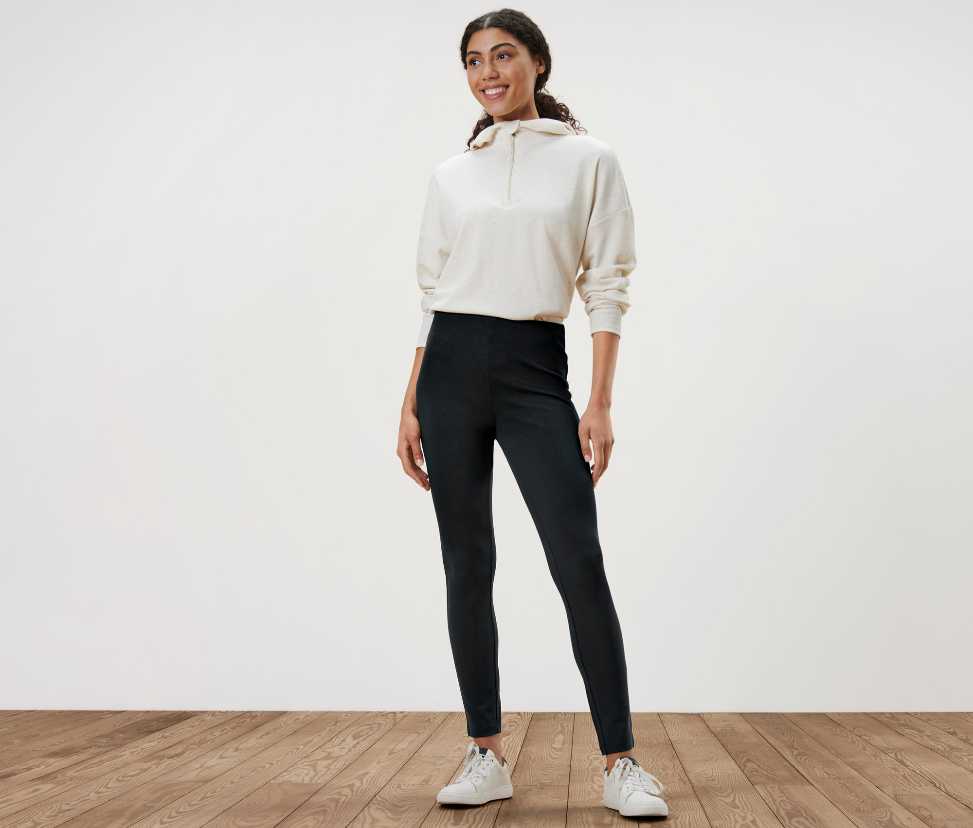 Une femme debout portant un legging lourd noir, un pull blanc et des baskets blanches.