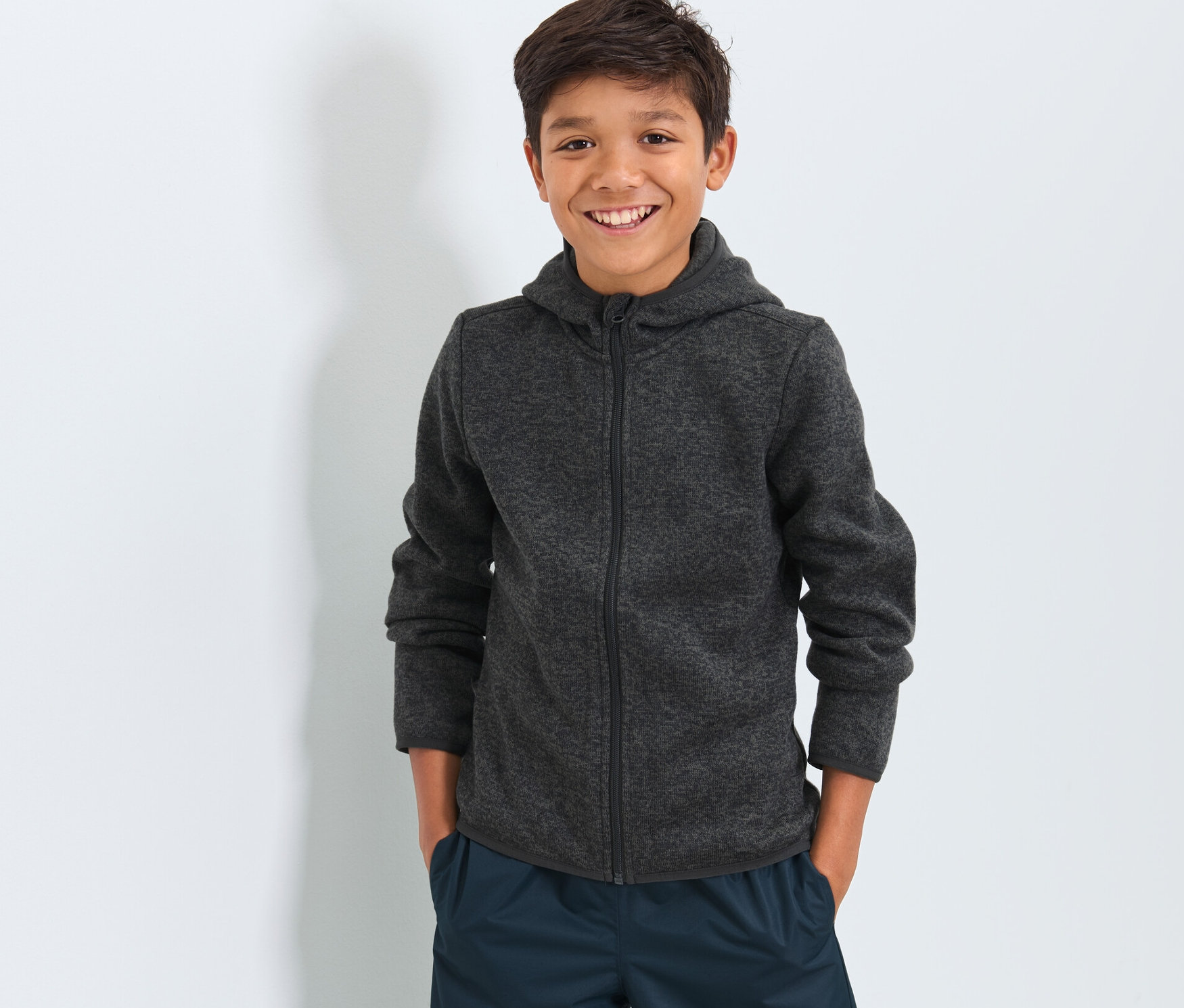 Un garçon porte une veste en maille polaire pour enfant et un pantalon bleu marine.