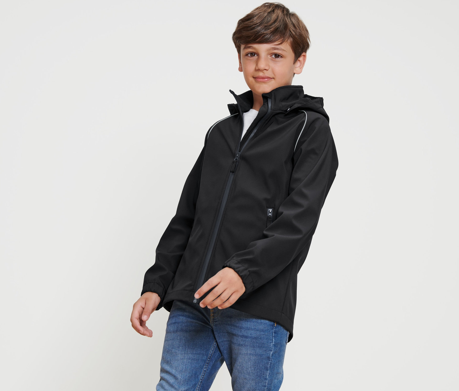 Un garçon pose portant une veste en softshell noire pour enfant.