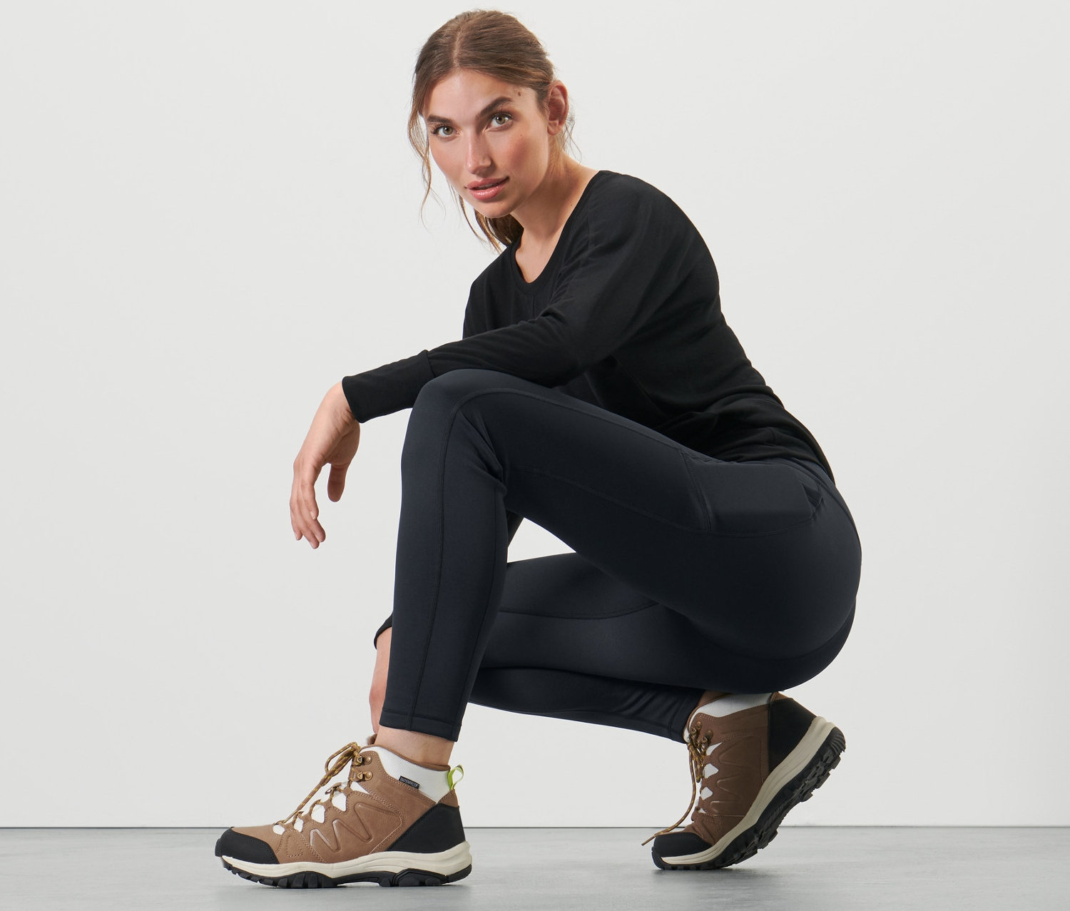 Femme accroupie portant un legging thermique noir et des bottes marron.