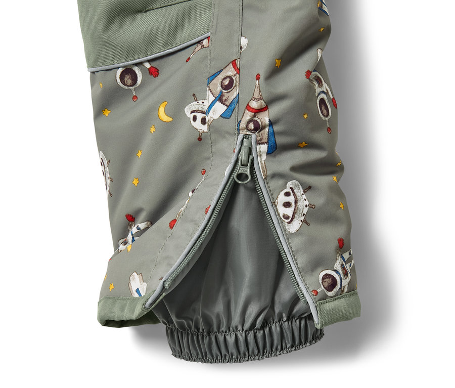 Détail d'une combinaison de ski pour enfant avec un imprimé de vaisseau spatial et une fermeture éclair ouverte.