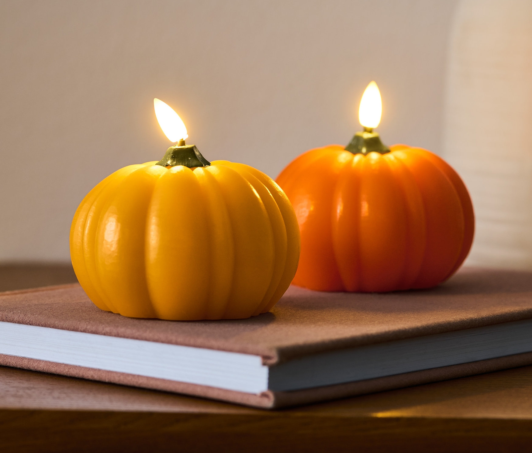 Deux bougies en cire véritable à LED « courge » sont posées sur un livre sur une table en bois.