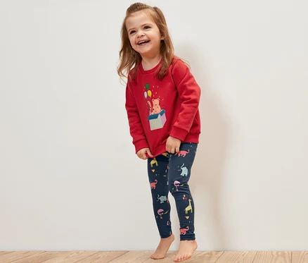 Fillette souriante portant un pull rouge et 5 leggings pour enfant avec des motifs d'animaux.