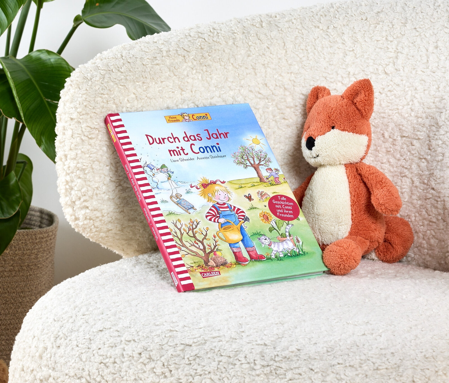 Le livre «Durch das Jahr mit Conni» est posé sur un fauteuil blanc à poils longs à côté d'un renard en peluche.
