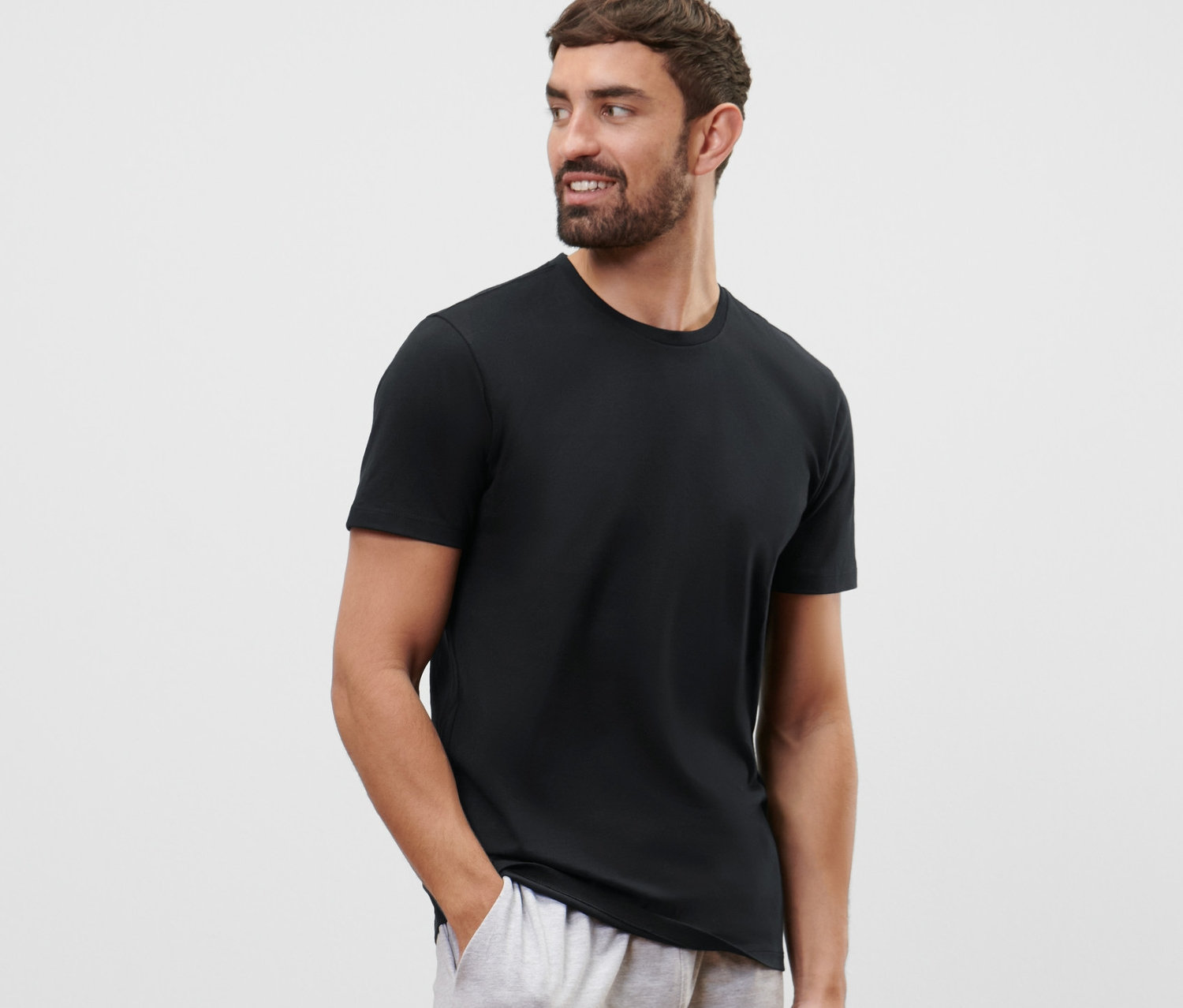 Un homme barbu porte un T-shirt noir à col rond de l'ensemble de 2 et un short gris.