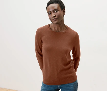 Une femme pose, portant un pull en maille fine mérinos couleur cognac et un jean.