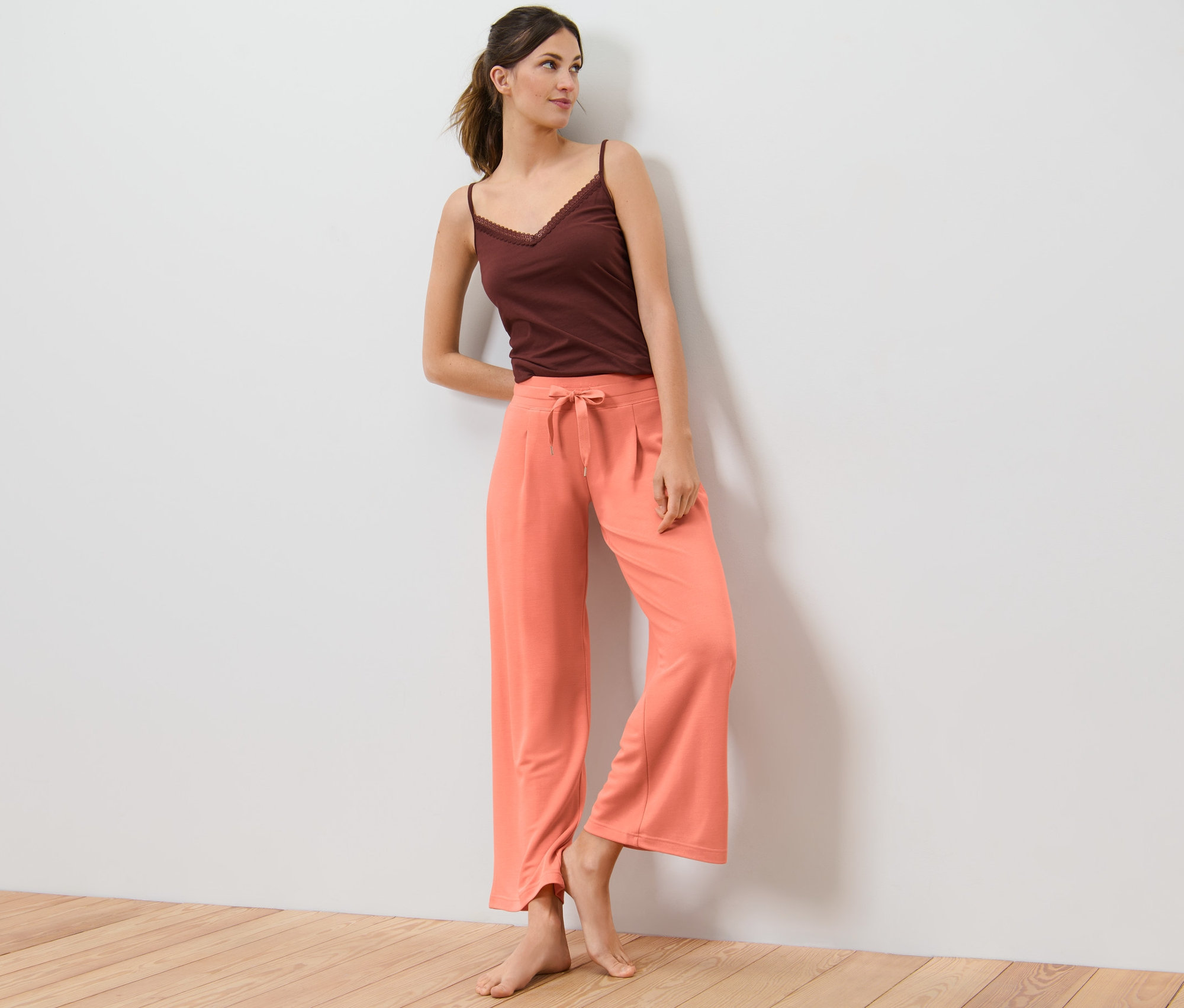 Femme appuyée contre un mur portant un pantalon d’intérieur et un haut marron.