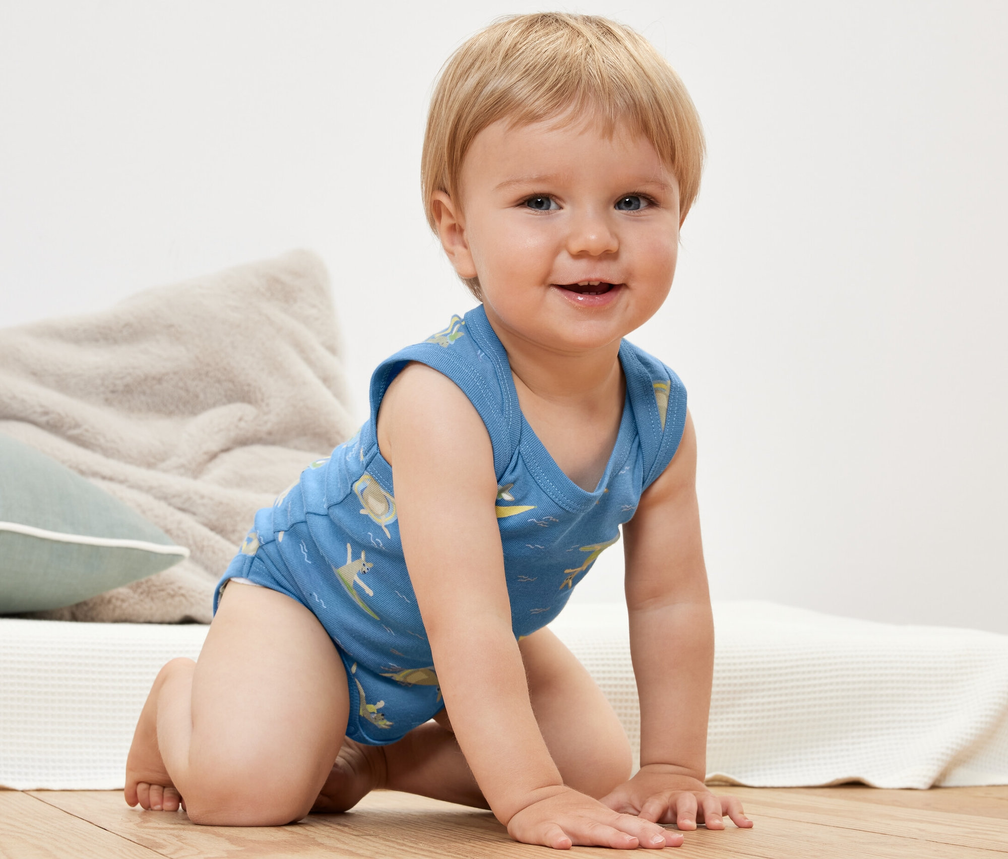 Un bébé souriant à genoux porte un 2 bodys pour bébé bleu imprimé.