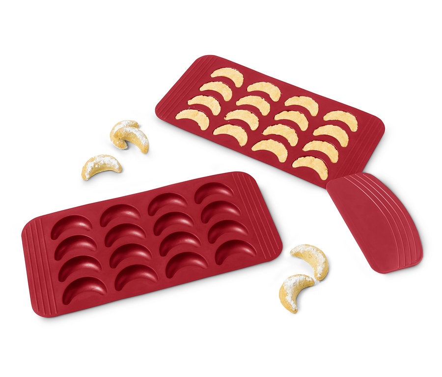 Deux feuilles de cuisson rouges pour croissants vanillés, une remplie de croissants cuits et quelques croissants à côté des feuilles.