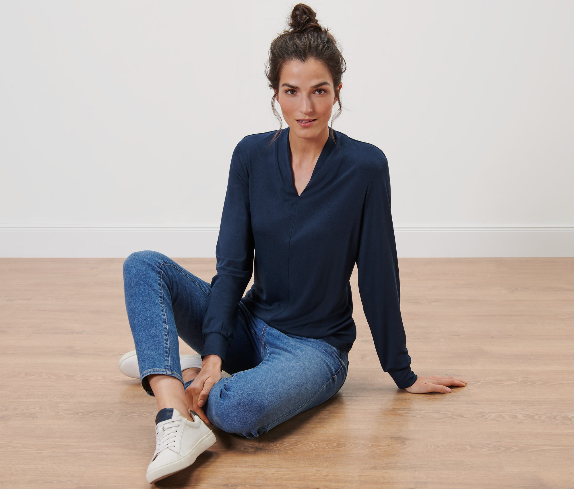 Femme assise par terre portant un t-shirt manches longues avec encolure en V, bleu foncé.