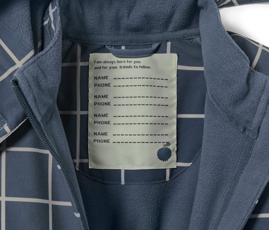 Détail d'une combinaison softshell à carreaux pour enfant avec une étiquette pour le nom et le numéro de téléphone.