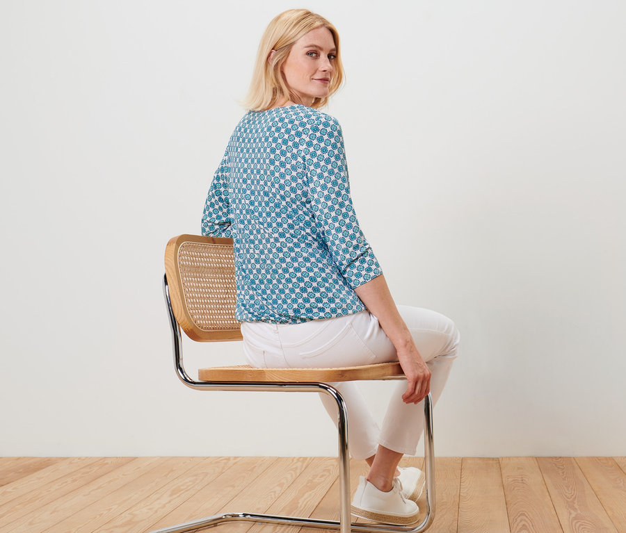Femme assise sur une chaise portant une blouse avec imprimé intégral.