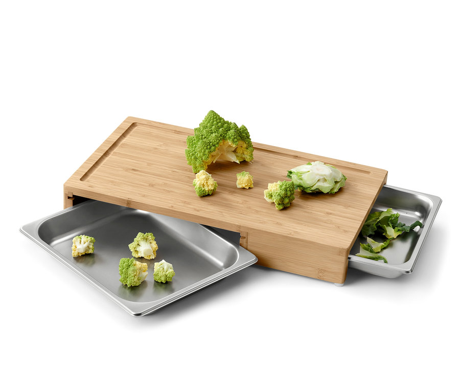 Planche à découper avec des légumes coupés et deux plateaux métalliques.