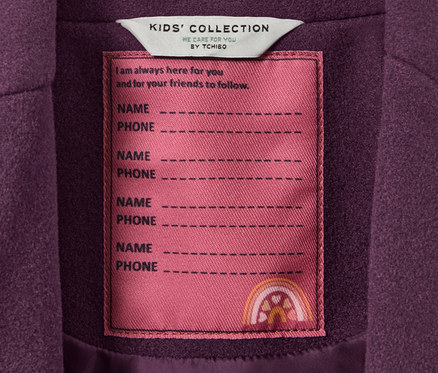 Gros plan sur un manteau pour enfant avec une étiquette KIDS' COLLECTION où l'on peut inscrire un nom et un numéro de téléphone.