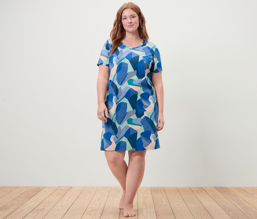 Une femme se tient pieds nus et porte une chemise de nuit à motifs géométriques bleus.