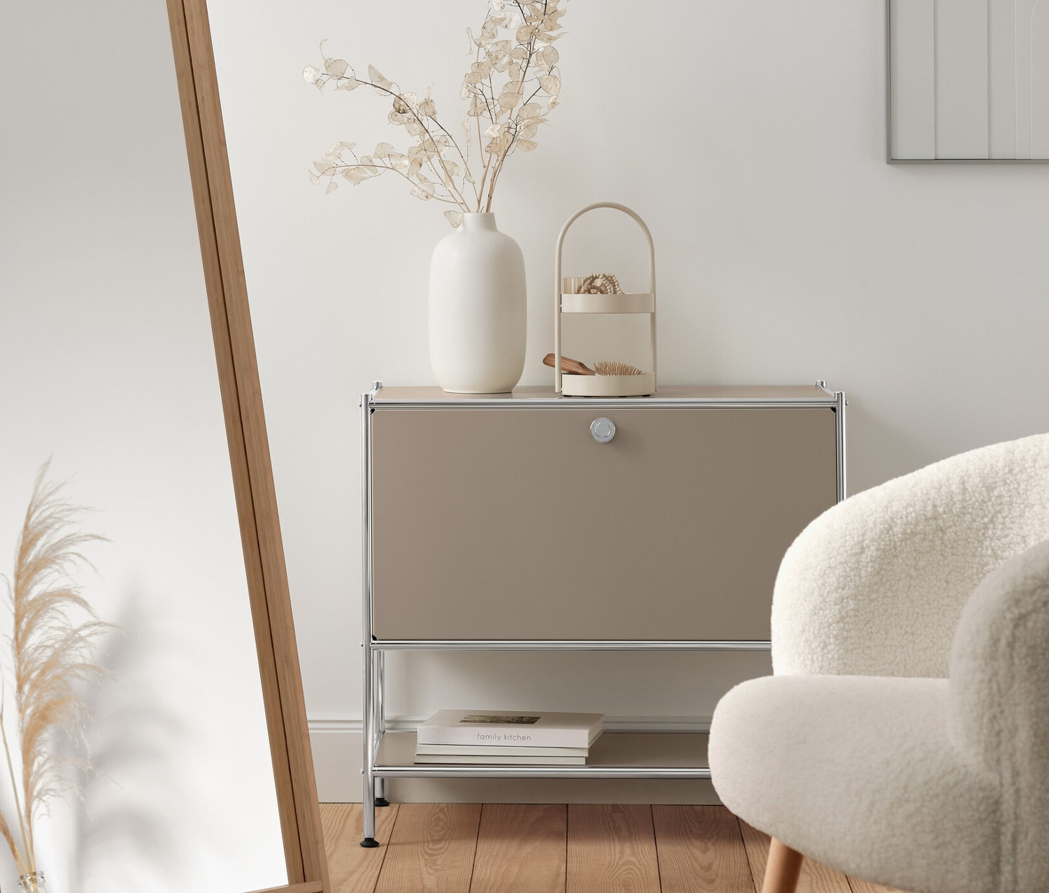 Intérieur avec buffet en métal « CN3 » beige avec abattant, miroir sur pied avec cadre en bambou et fauteuil bouclette avec pieds en bois.