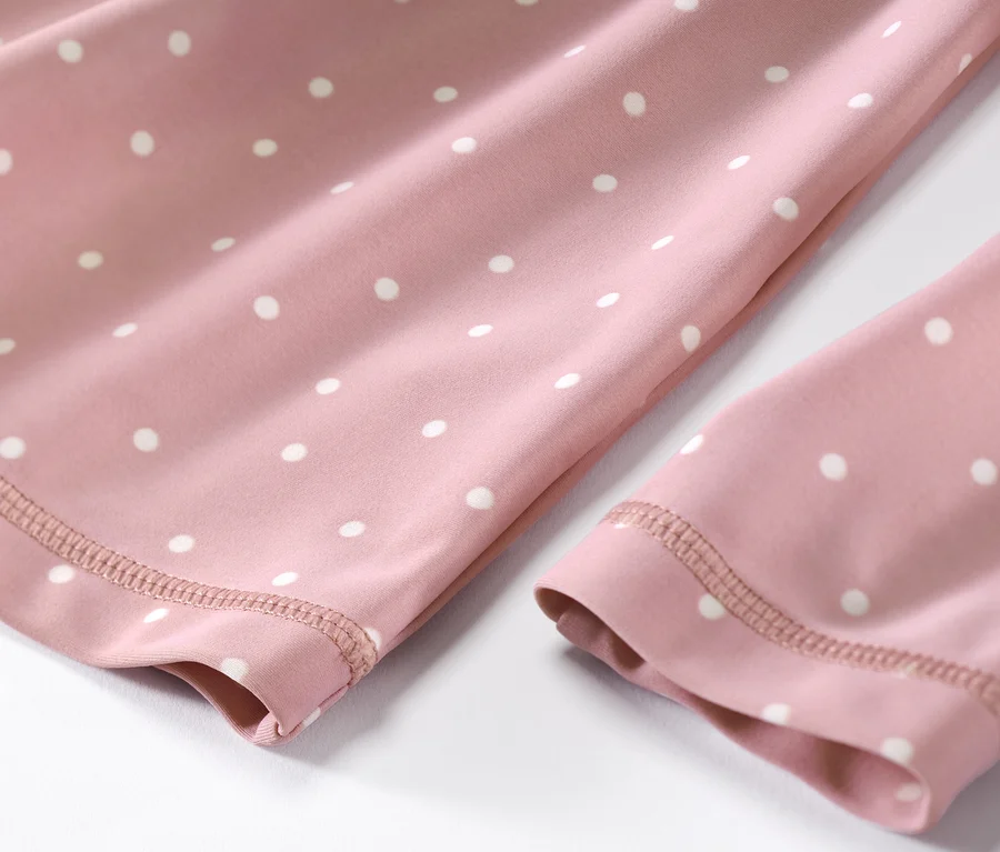 Gros plan sur un ensemble pour enfant avec protection UV 80, à pois blancs sur tissu rose.