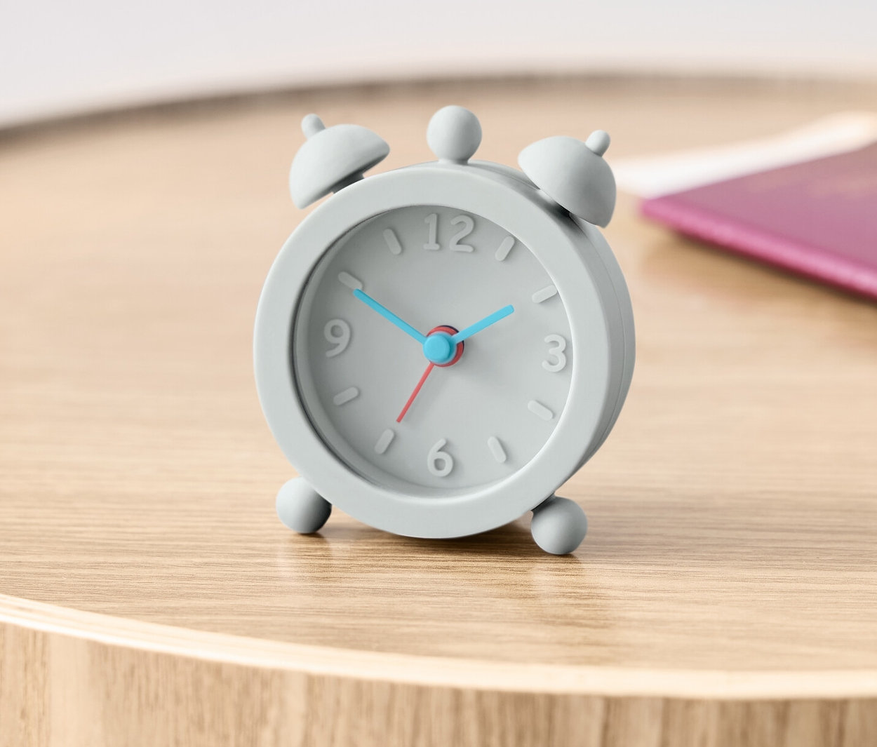 Un réveil de voyage gris est posé sur une table en bois à côté d'un passeport.