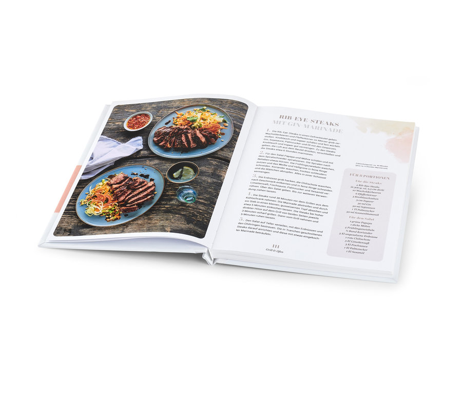 Un livre de cuisine ouvert montre deux assiettes de steak tranché et de salade à côté d'un bol de sauce.