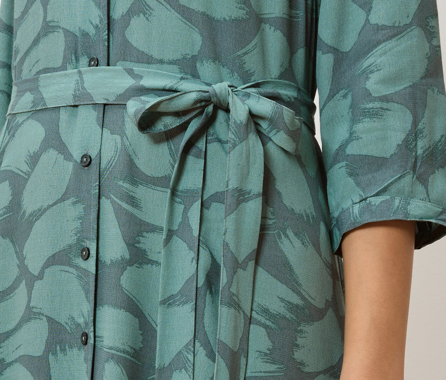 Détail d'une robe chemise turquoise à motifs de coups de pinceau gris et taille nouée.
