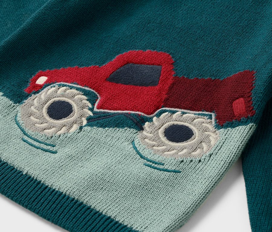 Gros plan sur un pull en maille pour enfant avec un motif de camion rouge.