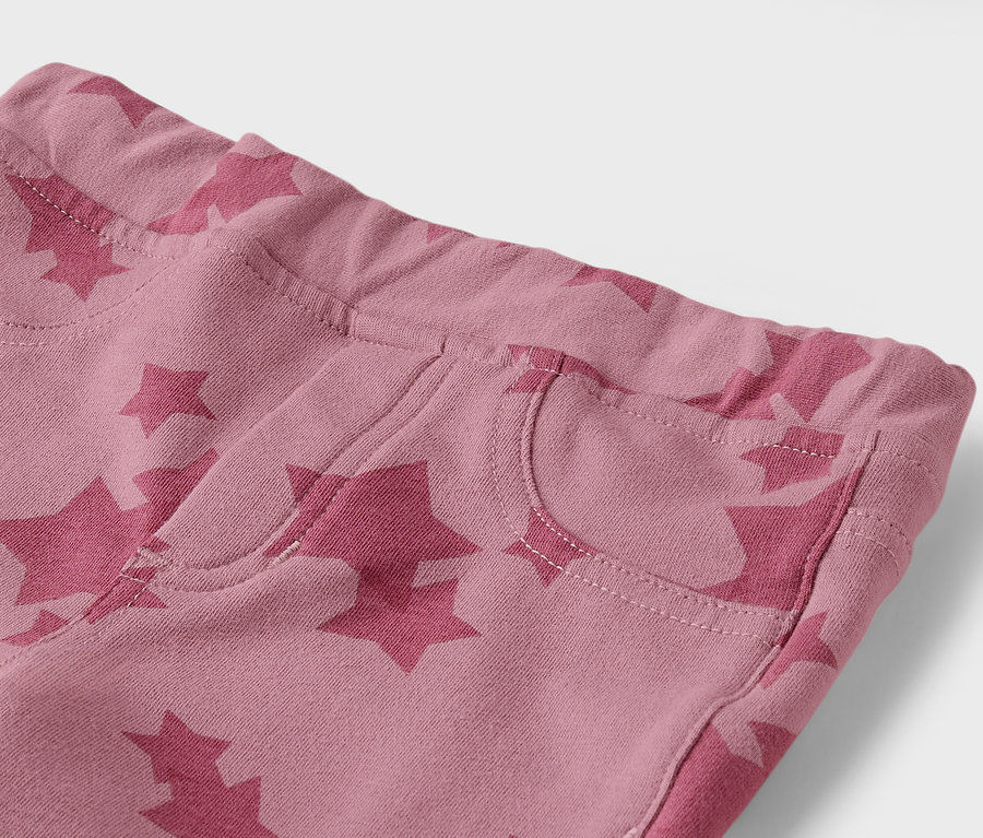 Détail d'un pantalon rose avec des étoiles et une poche.