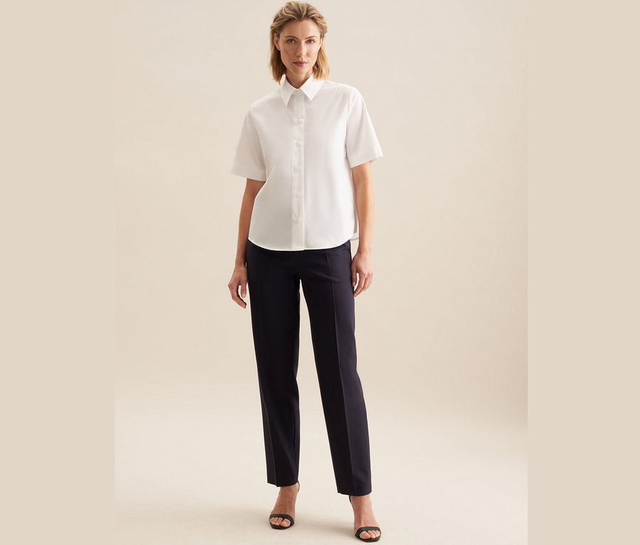 Femme portant un chemisier à manches courtes Seidensticker blanc et un pantalon bleu marine.