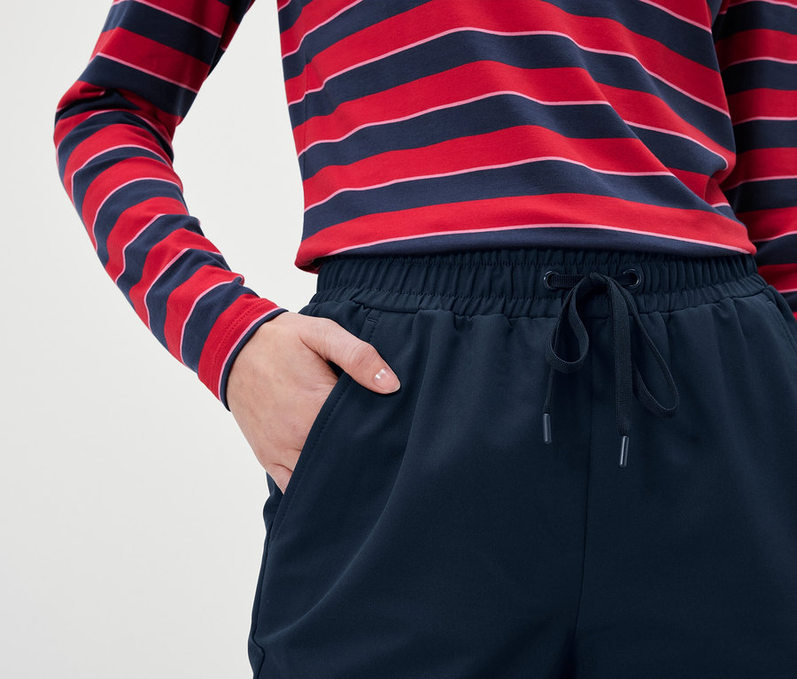 Gros plan d'une femme portant un pantalon de survêtement bleu marine et un t-shirt à manches longues rayé rouge et bleu avec une main dans la poche.